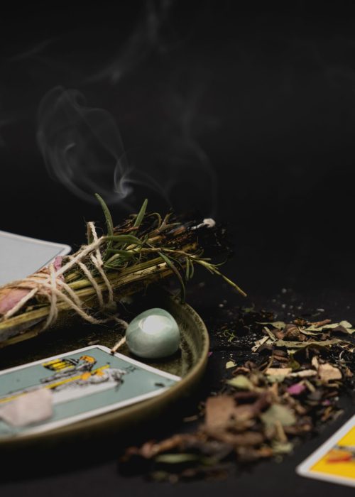 A spiritual still life with tarot cards, herbs, and crystals on a dark surface for meditation.