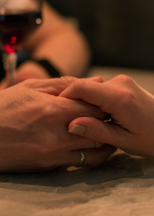 A romantic couple holding hands with a candle and wine glass in dim lighting, symbolizing love and intimacy.